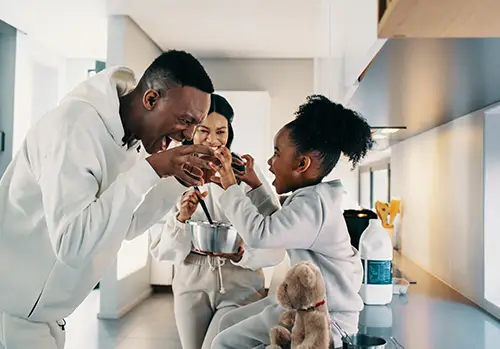 Dad playing with his daughter while mom is cooking in the kitchen