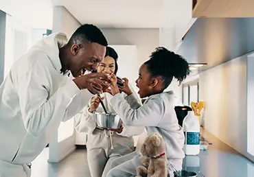 Dad playing with his daughter while mom is cooking in the kitchen