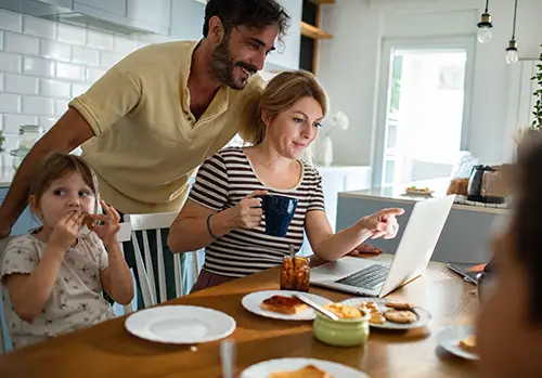 Mother working on laptop while family has breakfast in kitchen