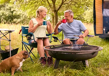 Senior Couple With Pet Dog Camping In RV Eating Breakfast Outdoors