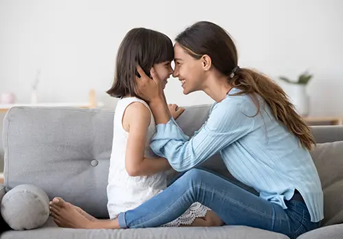 Mother and daughter smile and look into each others eyes as they press their foreheads together.