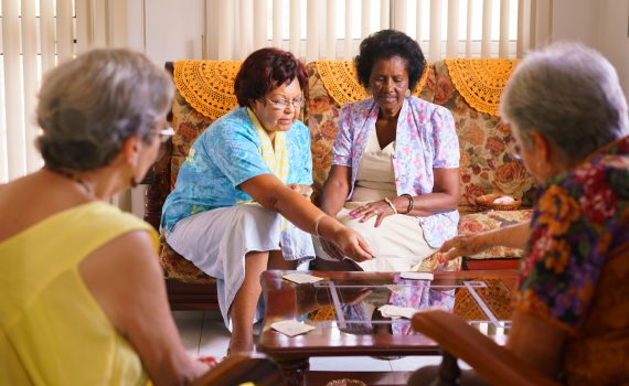 Old people in geriatric hospice: group of senior women playing cards and having fun together. The aged ladies sit on the sofa of the hospital and start a new match
