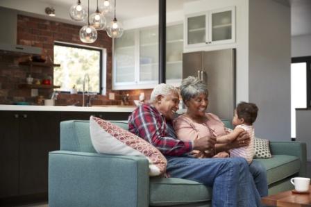 An older couple sit on their couch and smile as they hold their grandchild. They can provide for their grandchild and other family members by educating themselves on the myths and misconceptions of life insurance.