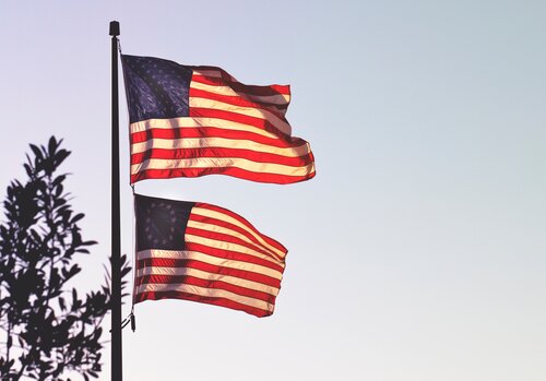 Two American flags wave on a flagpole.