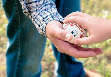 A sports parent is photographed handing a baseball to his child.