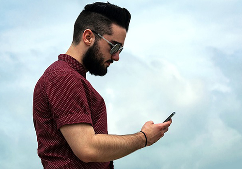 Man looking down at phone with a cloudy backdrop.