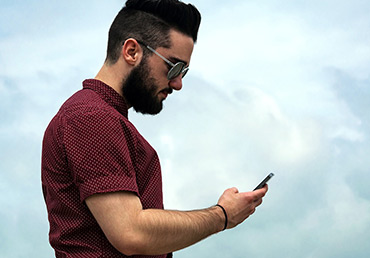 Man looking down at phone with a cloudy backdrop