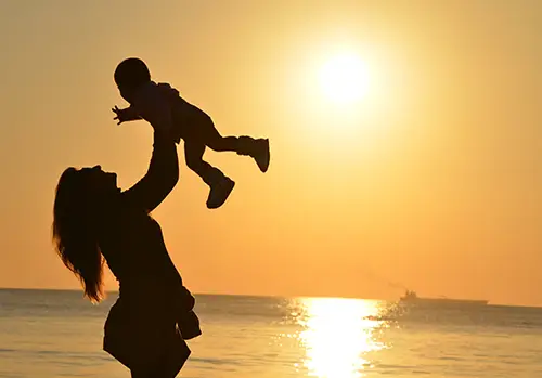 A woman holds her child at sunset.
