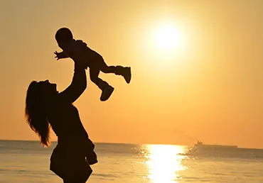 A woman lovingly holds her child at the beach.