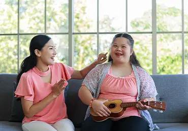 girl with special needs playing the guitar with her mom besides her