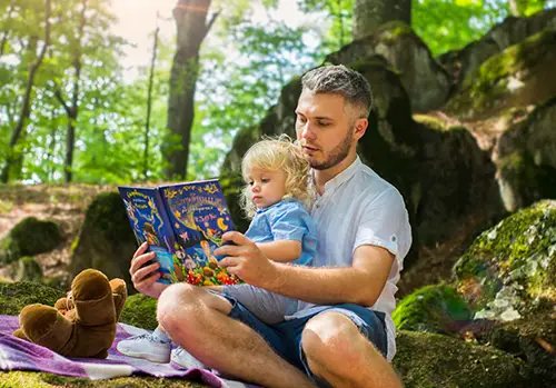 A father and daughter sit in the forest and read a story together.