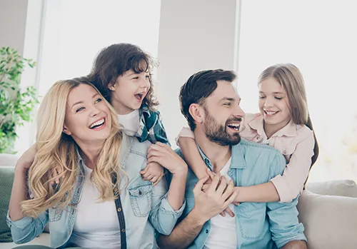 A family of four smiles and laughs together in their home.