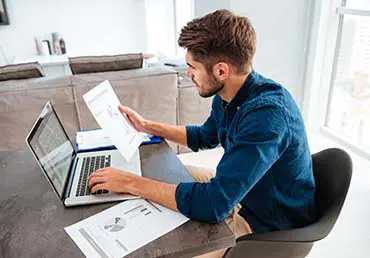 A young man analyzes his finances at his computer. Photo by Storyblocks.