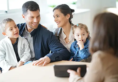 A family, consisting of a husband and wife and two young children, sit at a table with a life insurance agent.