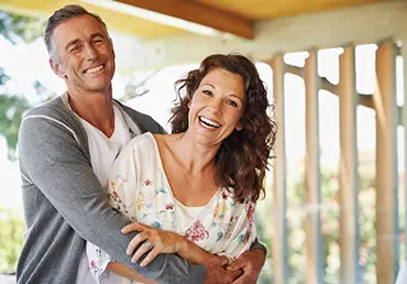 A happy husband and wife laugh together outside.