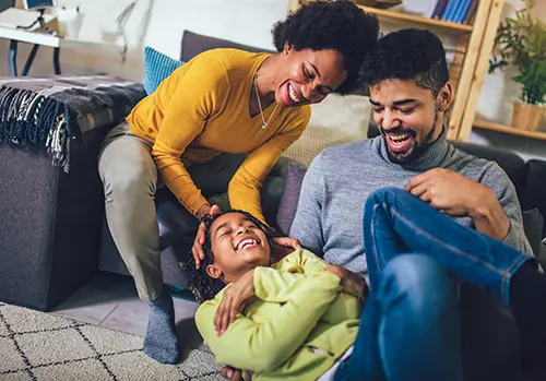 A mom and dad laugh together with their daughter in their home.