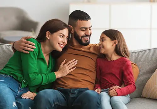 Young family sits on a couch and laughs with each other.