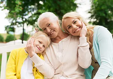 A woman, her senior mother, and her daughter sit together in the park for a photograph.