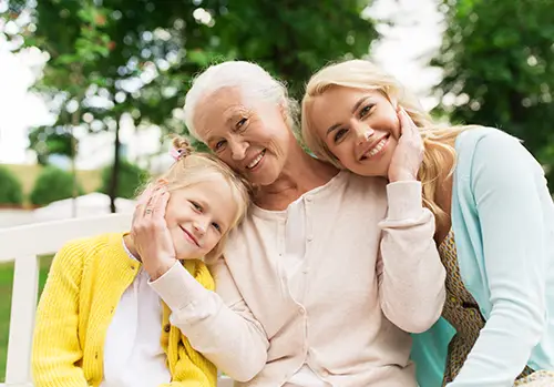 A woman, her senior mother, and her daughter sit together in the park.