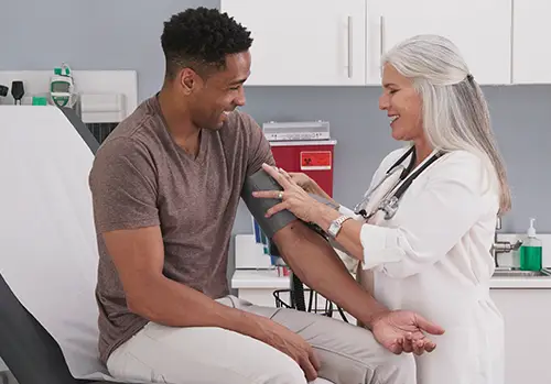 A doctor performs a blood pressure exam on a young man in her office.