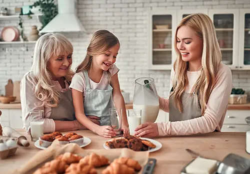 A grandmother, mother, and daughter bake and eat treats together in the kitchen.