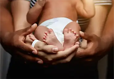 Close-up of a newborn baby wearing a diaper, gently supported by the hands of two parents, symbolizing protection, care, and financial insurance security for new parents.