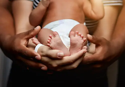 Close-up of a newborn baby wearing a diaper, gently supported by the hands of two parents, symbolizing protection, care, and financial insurance security for new parents.
