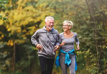 A smiling senior couple jog together in the park.