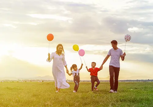 A family of four holds balloons as they walk together outside.