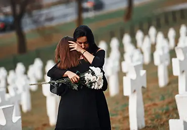 Two young women grieving together in a cemetery with white crosses, representing funeral and loss